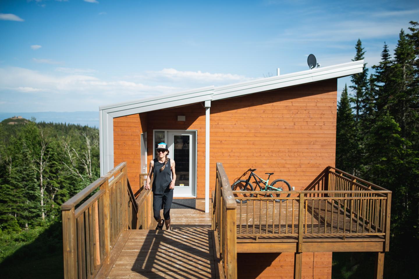Cabane en bois avec terrasse, vue sur la forêt, ciel bleu.