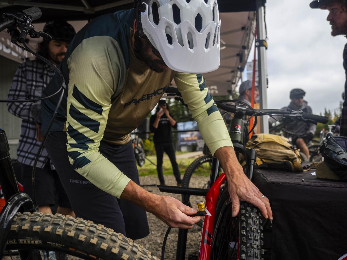 Personne vérifiant un pneu de VTT sous un auvent, portant un casque blanc.