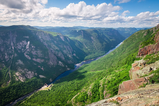 Vallée verdoyante et montagneuse avec rivière sinueuse sous un ciel partiellement nuageux.